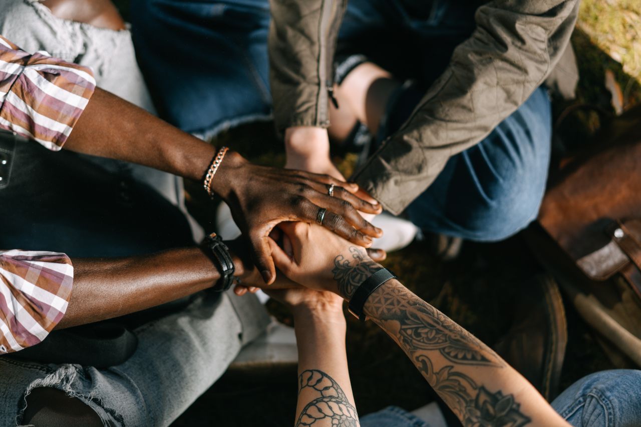 About A diverse group of individuals uniting in solidarity with hands stacked together outdoors.